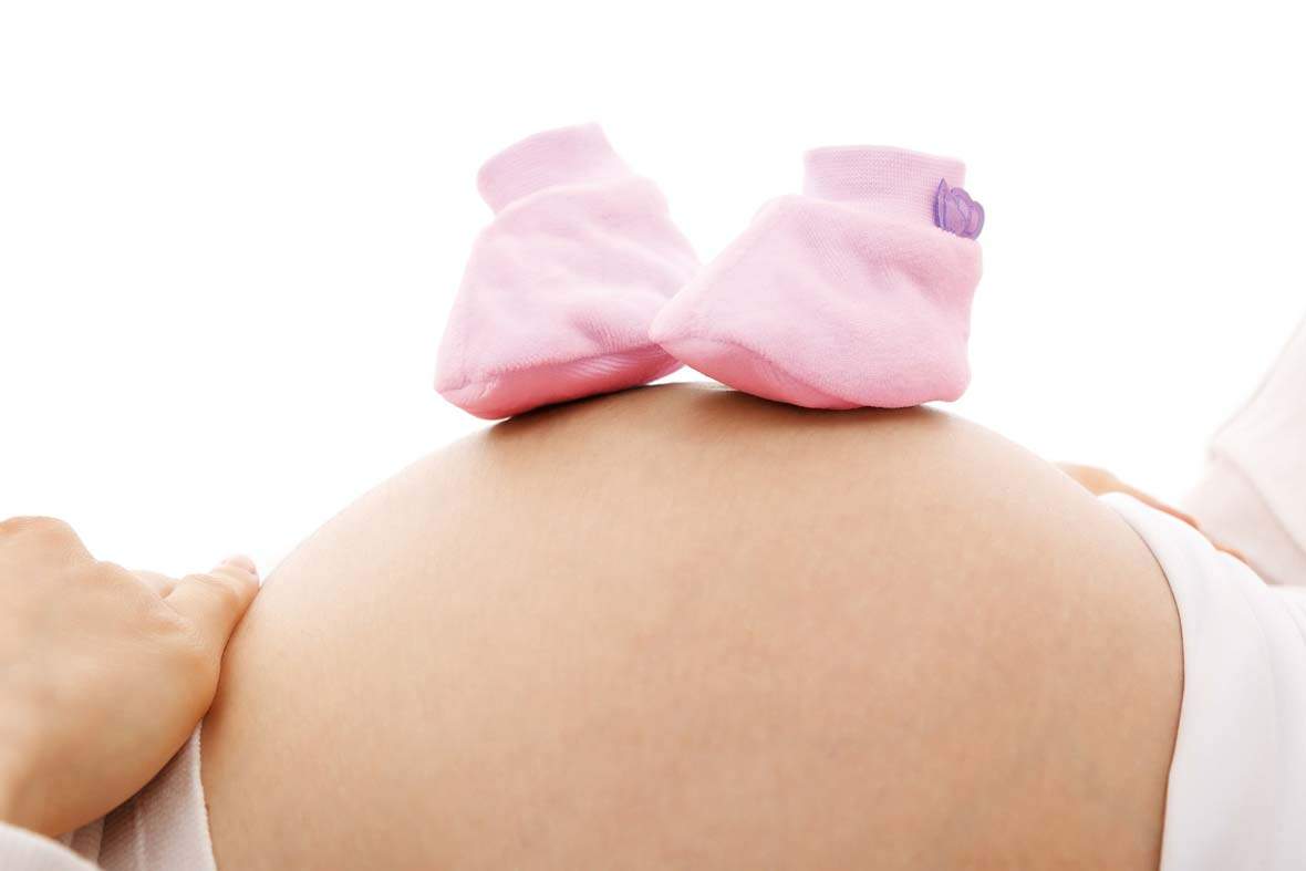 schwangerschaft, frau liegt mit ruecken auf dem boden und hat 2 kleine schuhe auf dem grossen, runden bauch